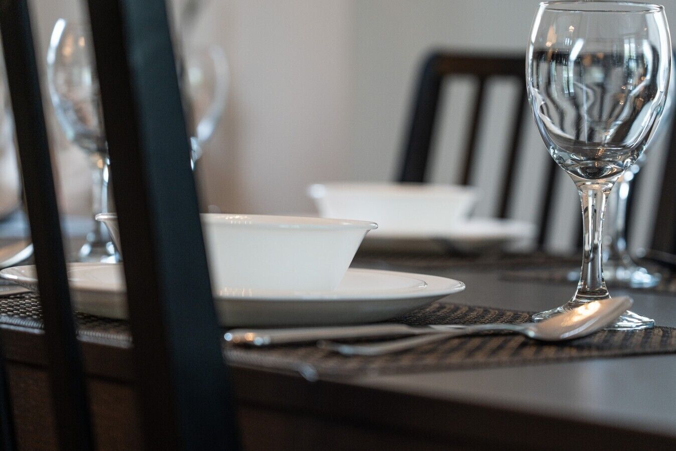 A dining table with a white bowl and a wine glass, set on a woven placemat.