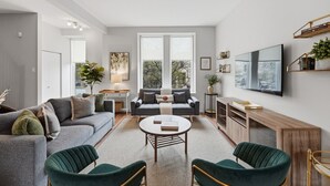 Een moderne woonkamer met een grijze bank, een ronde salontafel en twee groene fauteuils.