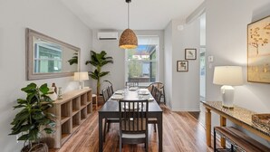 Een eetruimte met een lange tafel, stoelen, een hanglamp en een groot raam.