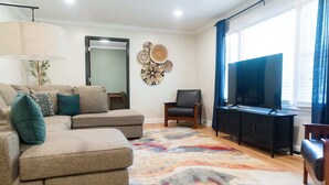 A living room with a sectional sofa, a flat-screen TV, a cabinet, and a colorful rug.