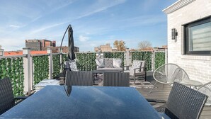 Une terrasse extérieure avec une table et des chaises, une pergola et une vue sur les bâtiments en arrière-plan.