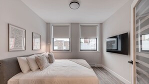 Une chambre à coucher avec un lit, deux fenêtres, un téléviseur à écran plat et des œuvres d’art encadrées accrochées au mur.