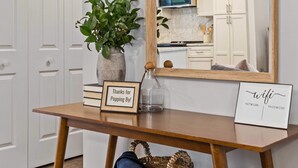 A wooden console table with a mirror, a potted plant, a framed sign, and a wicker basket. - Upscale Raleigh Retreat | Pet-Friendly | Back Deck (Raleigh)