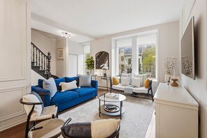 Una sala de estar con un sofá azul, un sofá blanco, una mesa de centro y una escalera.