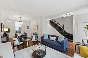 Amplia sala de estar con sofá azul, comedor, escalera y una lámpara de araña moderna.