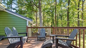 A deck with Adirondack chairs and a table, surrounded by a wooden railing, overlooking a forested area.