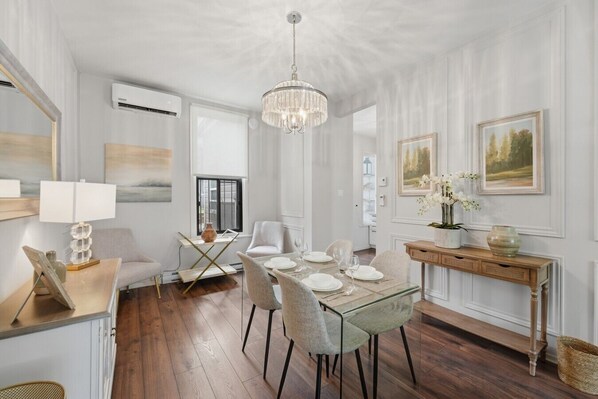 A dining area with a glass table, white chairs, a chandelier, and framed artwork on the walls.