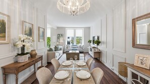 Ein Essbereich mit einer Chandelüster, einem für vier gedeckten Tisch und Blick in das Wohnzimmer.