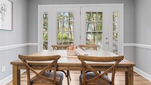 A dining room with a wooden table and chairs, a white door with glass panels, and a framed picture on the wall.