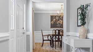 A dining area with a wooden table and chairs, a chandelier, and a painting on the wall.