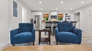 A modern living room with two blue armchairs, a wooden coffee table, and a kitchen in the background. - Fenced In|Updated|Pets OK|3 Bed 2 Bath|Walkable DT (Zebulon)