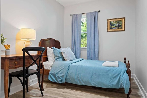 Une chambre à coucher avec un lit en bois, un bureau avec une lampe et une fenêtre avec des rideaux.