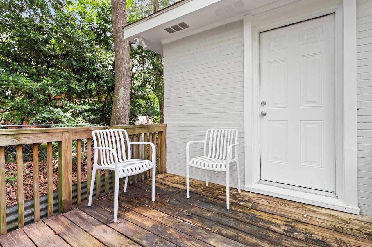 A wooden deck with two white plastic chairs and a white garage door.