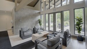 Ein modernes Wohnzimmer mit großem Fenster, grauen Sofas, einem Couchtisch und einer Topfpflanze.
