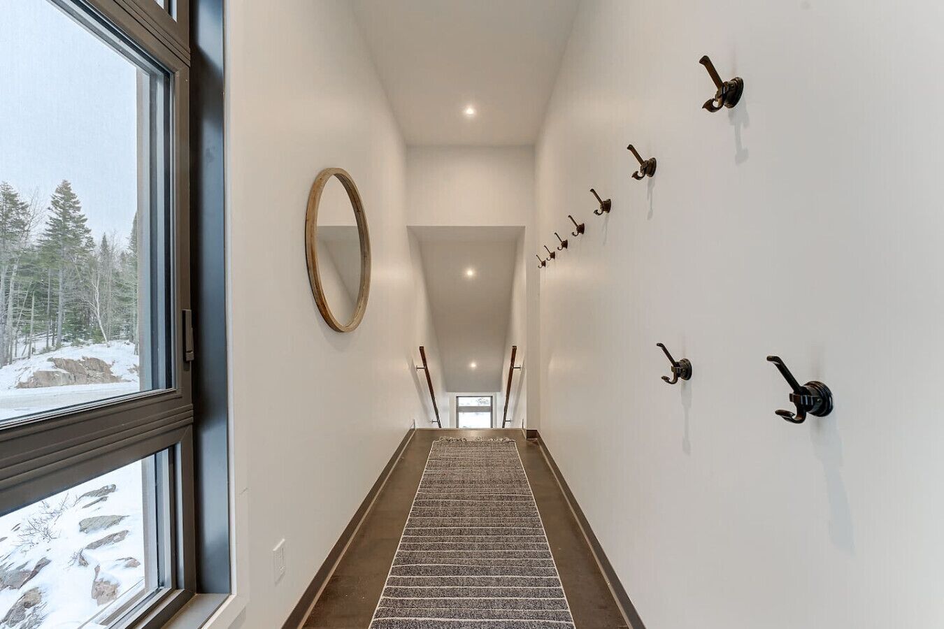 A hallway with a wooden floor, a large mirror on the left, and several wall-mounted hooks on the right.