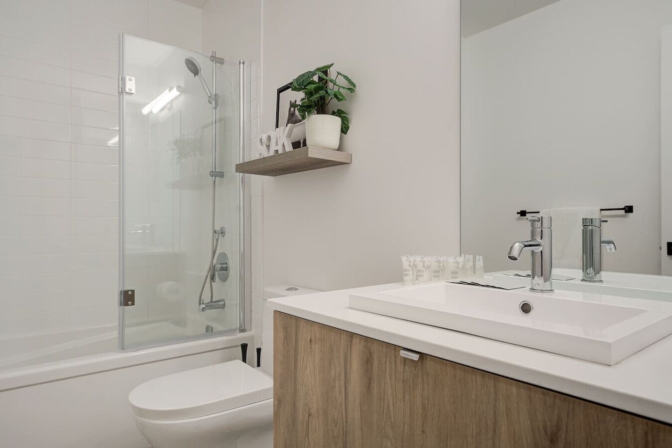 Une salle de bain moderne avec une douche à parois de verre, un lavabo blanc avec un meuble en bois, et un miroir au-dessus du lavabo.