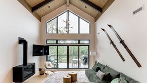 Ein geräumiges Wohnzimmer mit großem Fenster, Kamin, einer Couch und Skiern an der Wand.