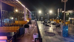 An outdoor dining area with yellow and black chairs, a wooden bench, and a sign for 'Night Manager'. - Syrus Hotel  (Mathura)