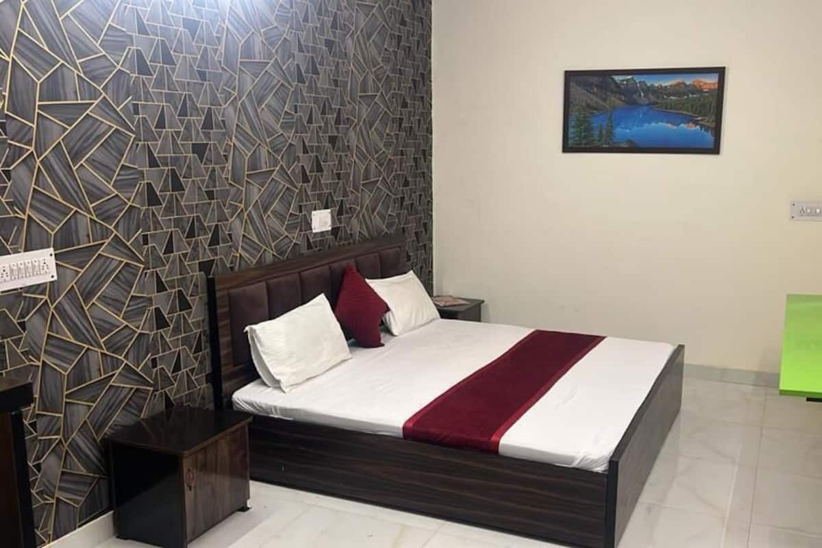 Un dormitorio con cama, mesita de noche, una mesa verde, televisor y pared con diseño geométrico.