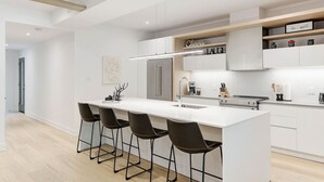 A modern kitchen with a central island, bar stools, a refrigerator, and built-in cabinets.