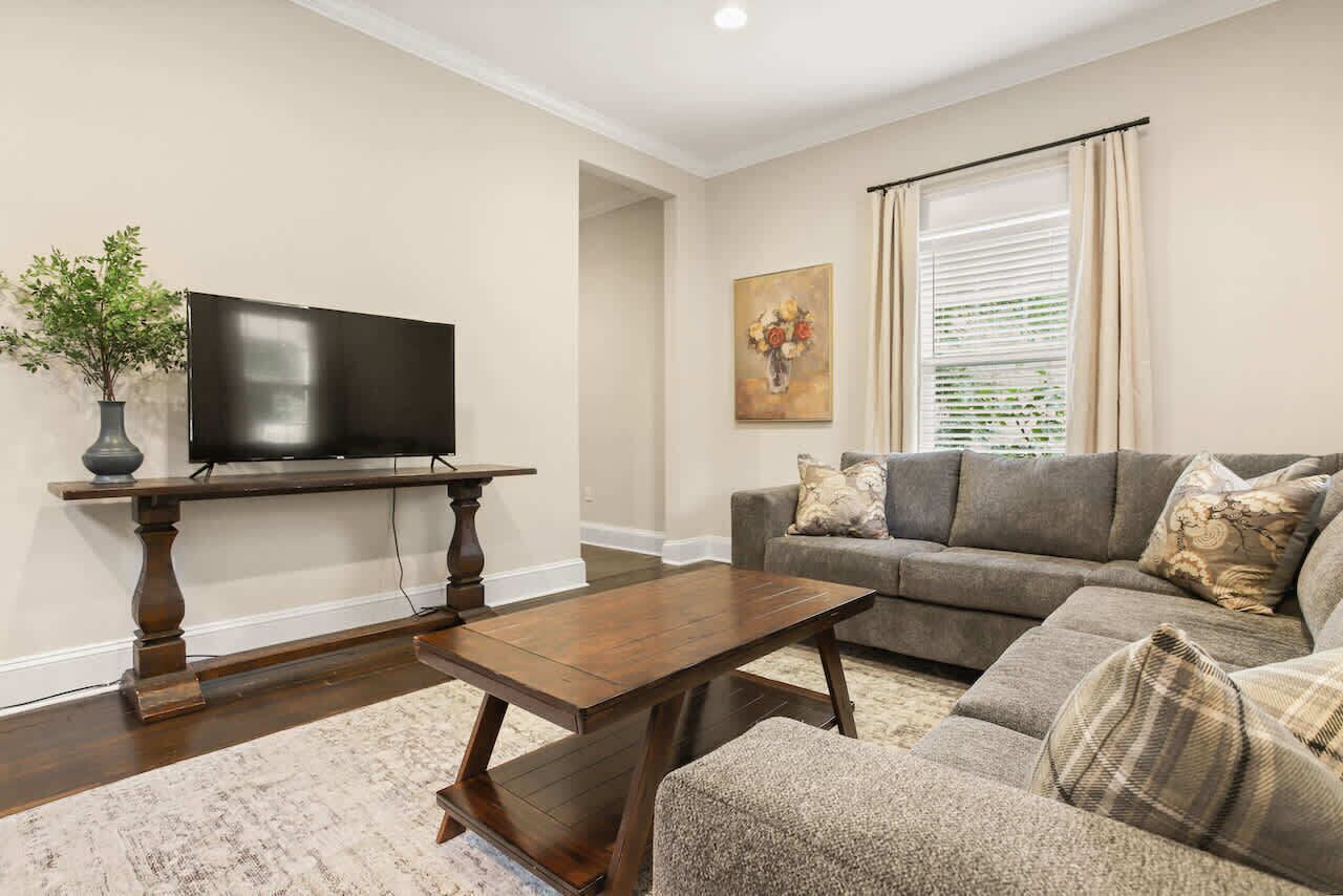 A living room with a flat-screen TV, dark wooden coffee table, and a grey sofa with patterned cushions.