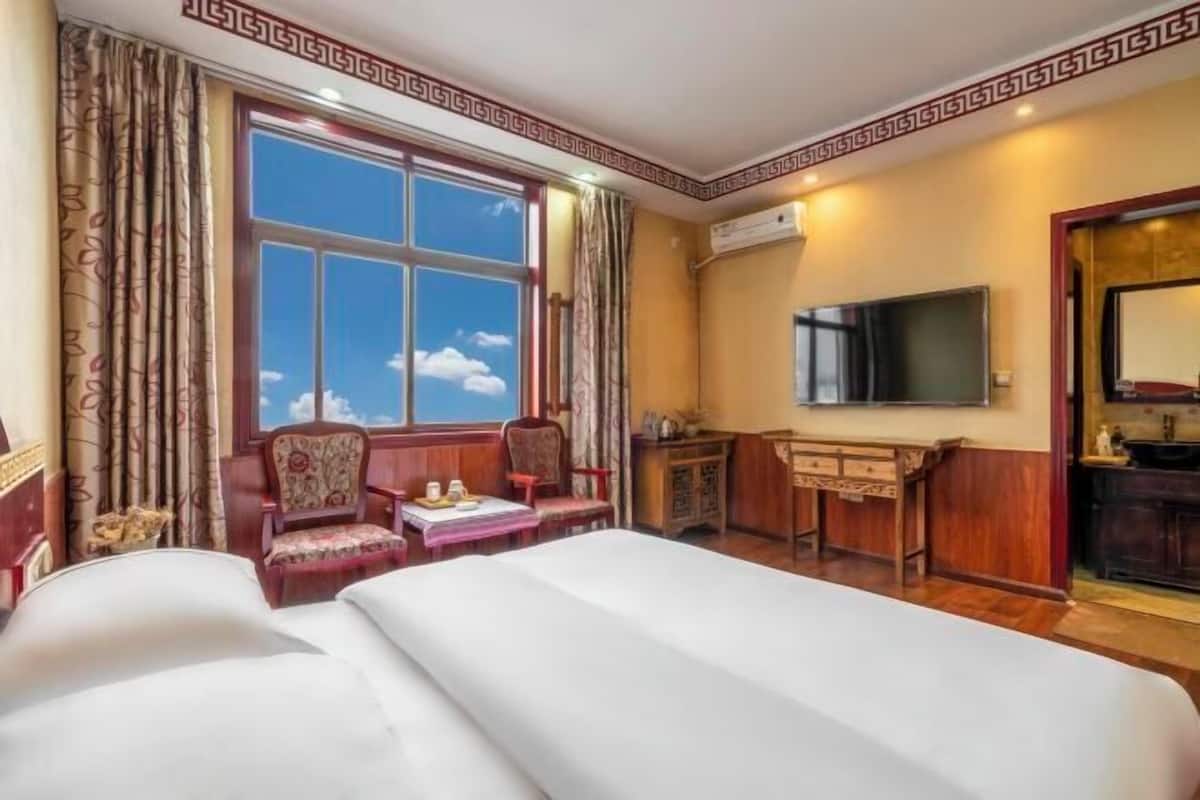 Une chambre d’hôtel avec un grand lit, un bureau, une chaise, une télévision et une fenêtre avec des rideaux.