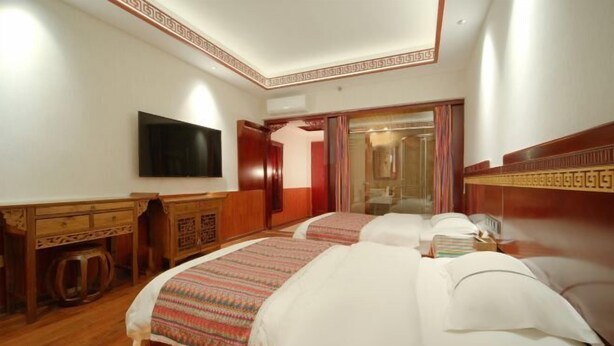 Quarto de hotel com duas camas, uma televisão e uma cômoda de madeira.