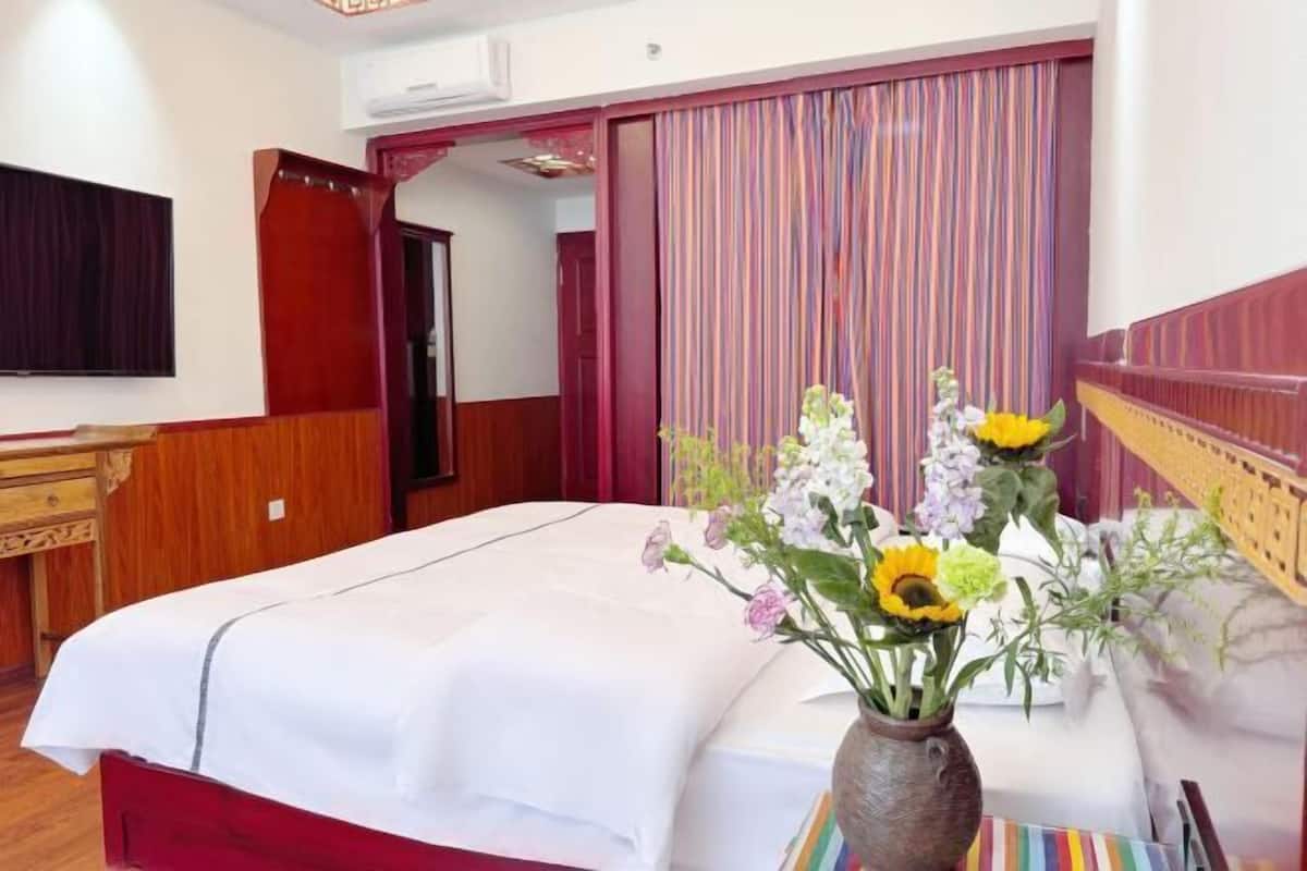 Une chambre d’hôtel avec un lit, une table de chevet en bois, un vase de fleurs et un rideau à rayures.