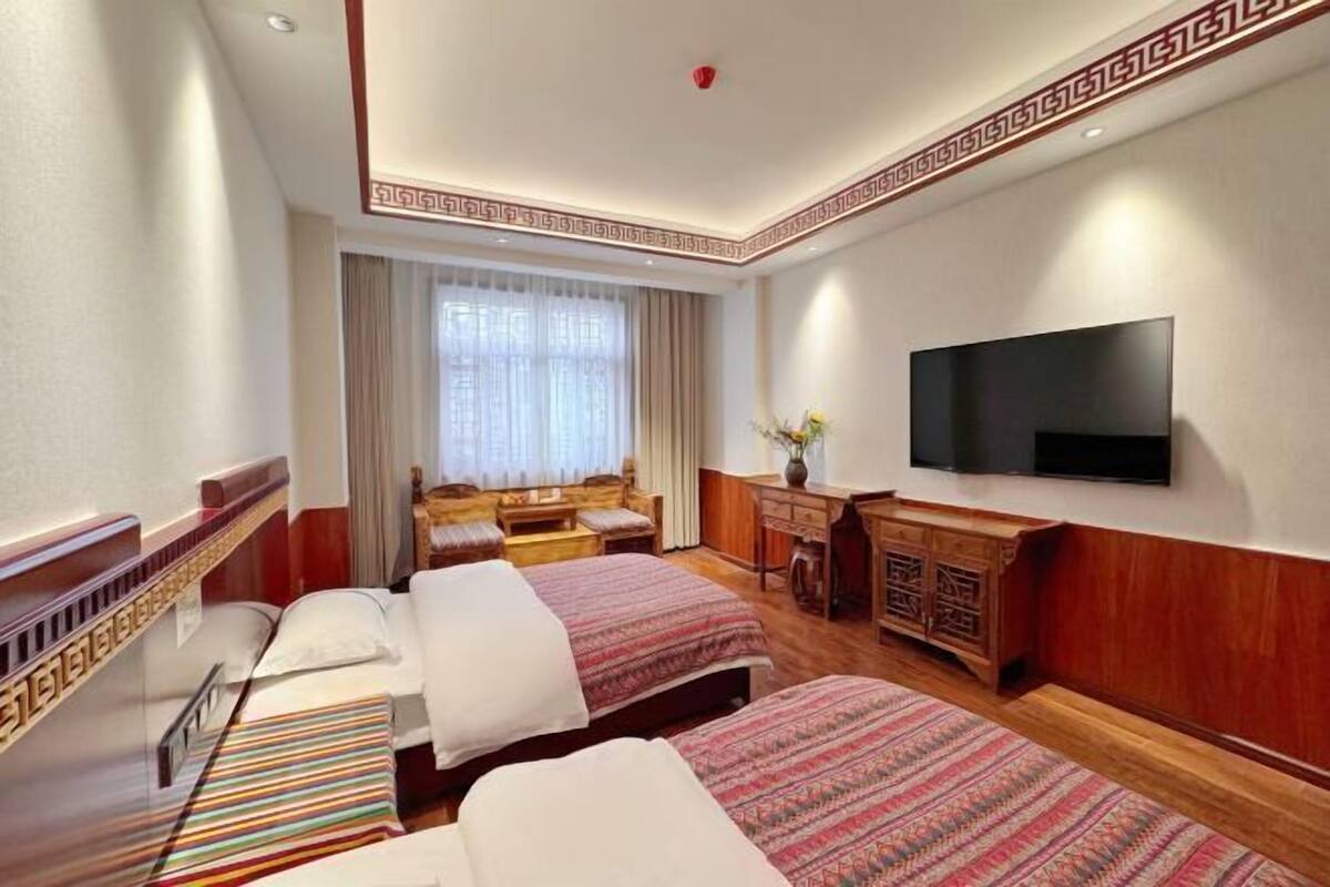 Une chambre d’hôtel avec deux lits, une télévision, un bureau et une fenêtre avec des rideaux.
