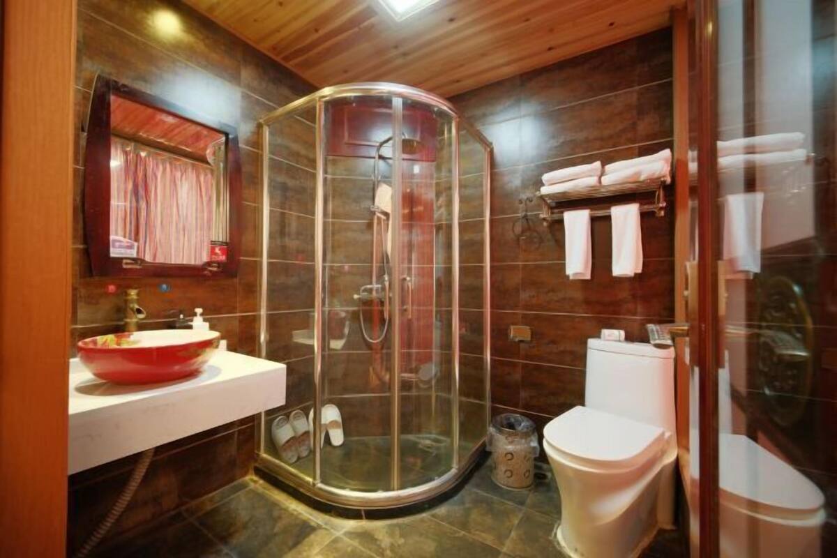 Une salle de bain avec une douche à parois de verre, des toilettes blanches, un lavabo rouge et un miroir au-dessus du lavabo.