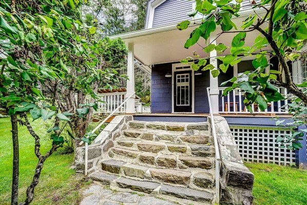 Une maison avec un escalier en pierre menant à un porche, le tout entouré de verdure.