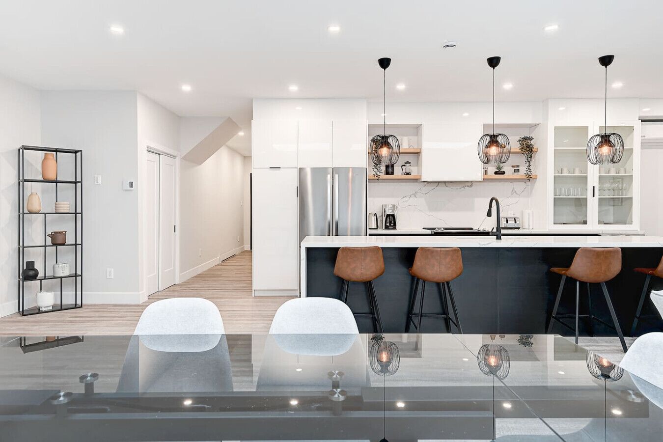Une cuisine moderne avec des meubles blancs, un îlot central doté de tabourets et un éclairage suspendu.