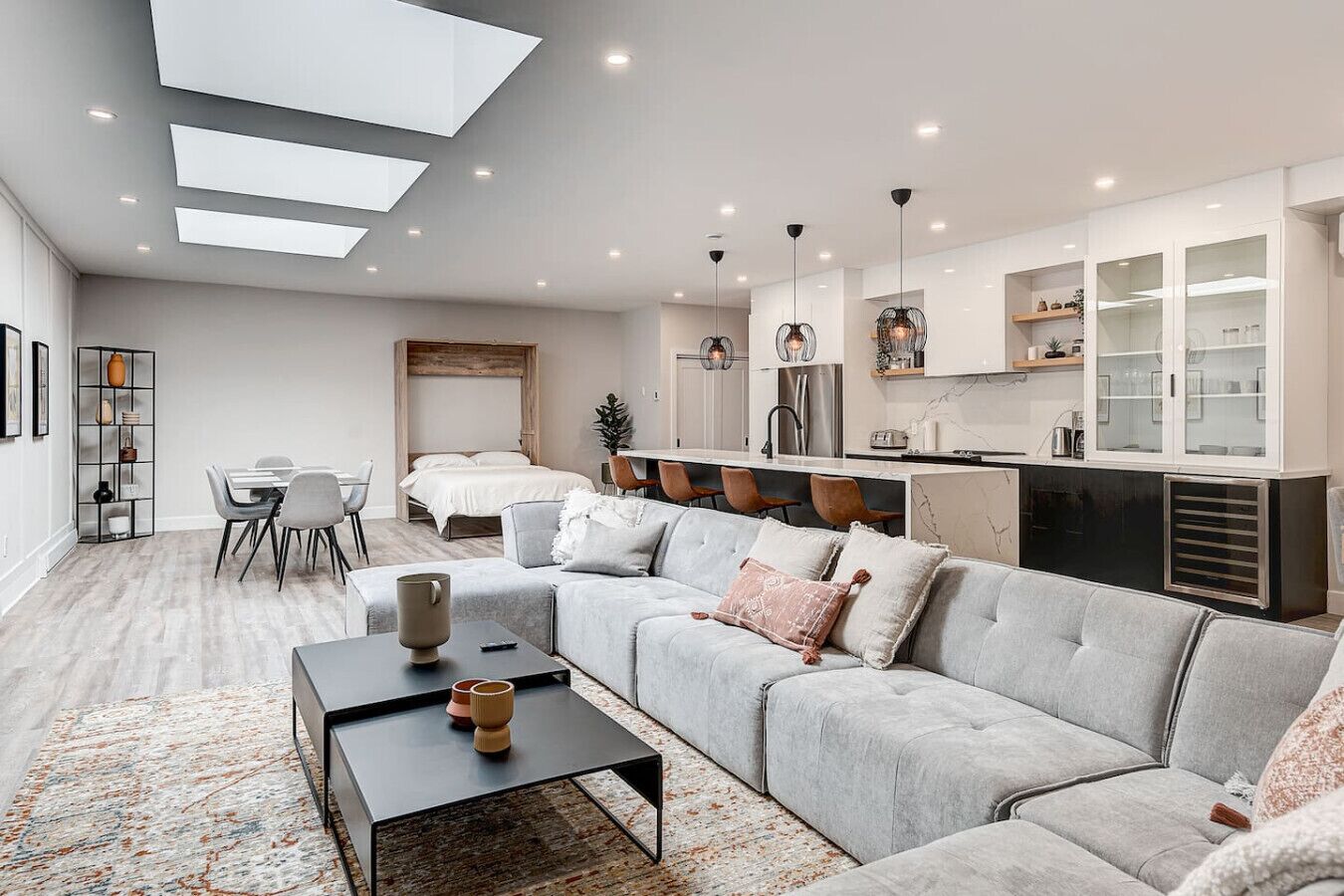 Un salon moderne avec un canapé gris, une table basse et un coin repas comprenant une table et des chaises blanches.