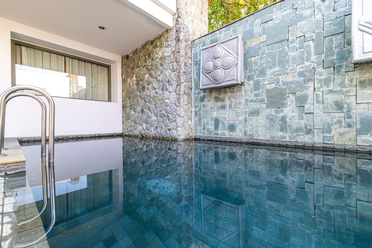 Un baño moderno con pared de piedra, cabina de ducha de vidrio y barandilla metálica.