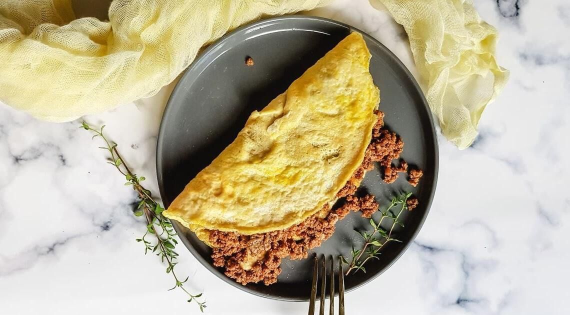 En tallrik med en hopvikt omelett och färs, tillsammans med en gaffel och en gul servett.