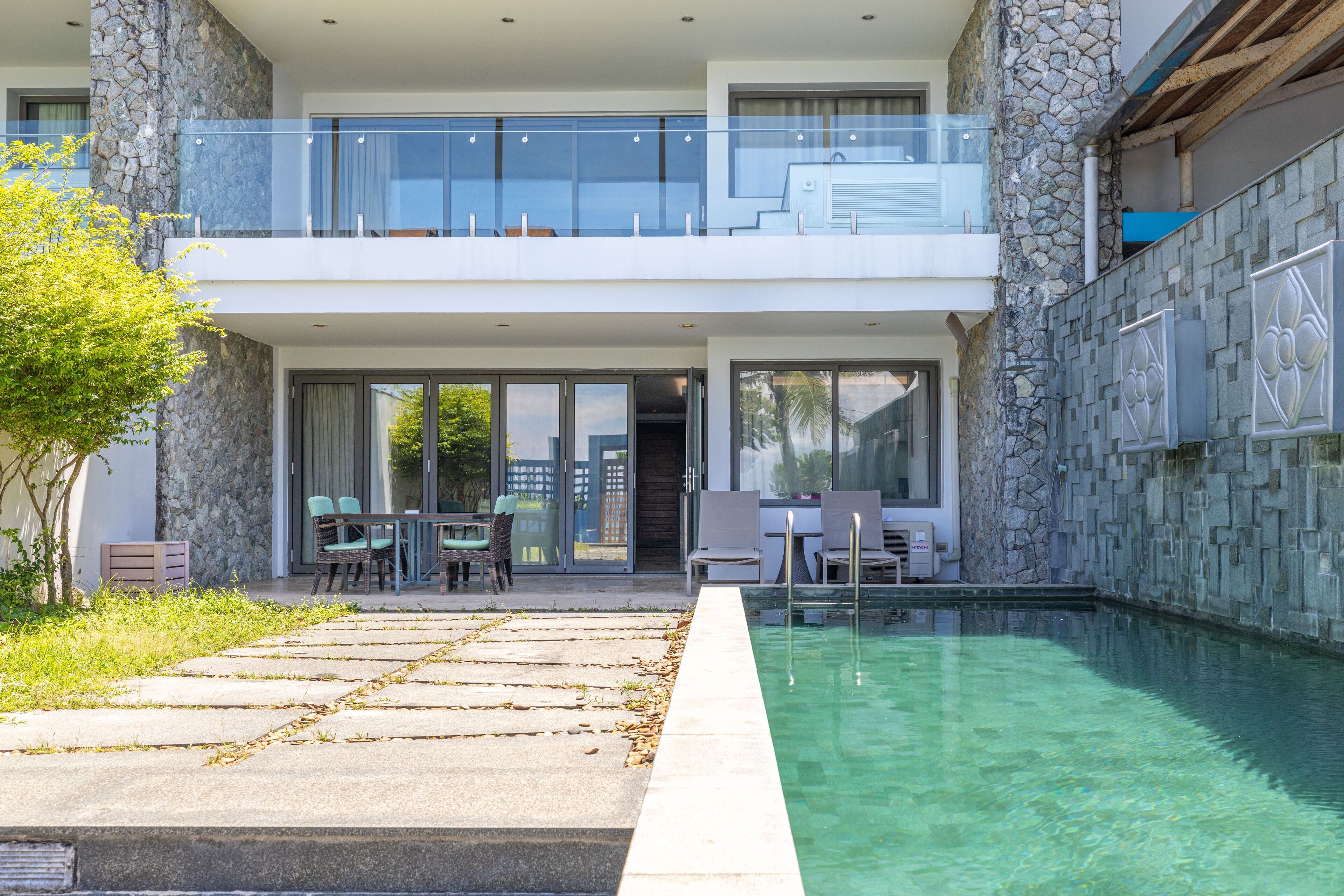 Un moderno edificio de dos plantas con fachada de piedra, un balcón de cristal y una piscina.
