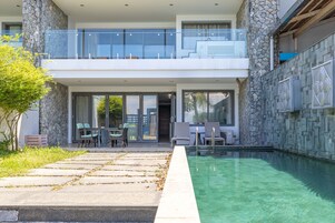 Un moderno edificio de dos plantas con fachada de piedra, un balcón de cristal y una piscina.