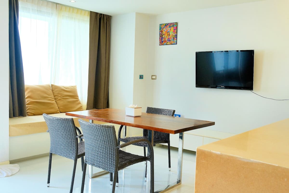 Una sala de estar moderna con sofá, mesa de comedor de madera, sillas de mimbre, televisor de pantalla plana y un cuadro en la pared.