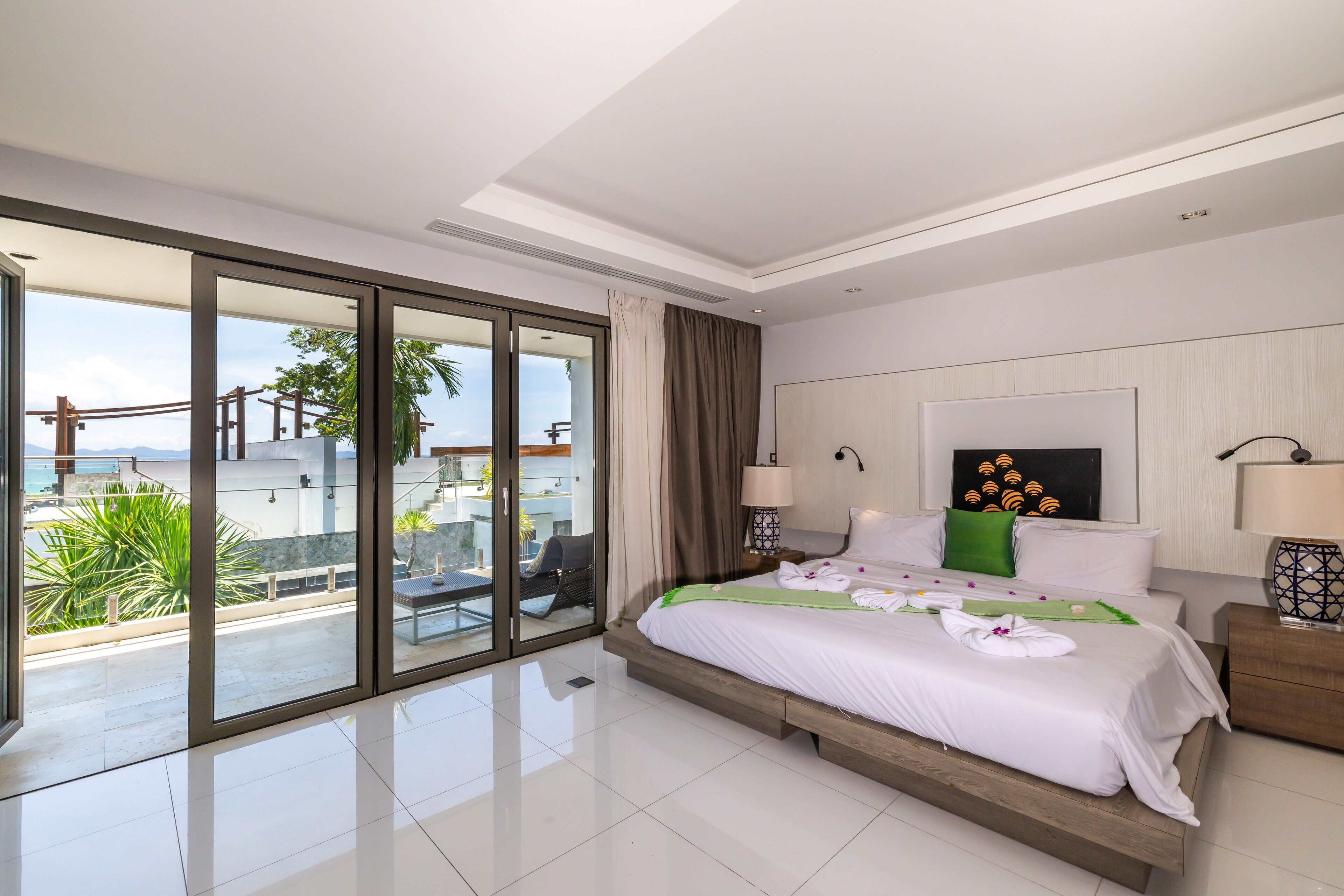 Ein modernes Hotelzimmer mit einer großen Schiebeglasdoor zum Balkon, einem ordentlich bezogenen Bett mit weißer Bettwäsche und Blick auf die Stadtlandschaft.