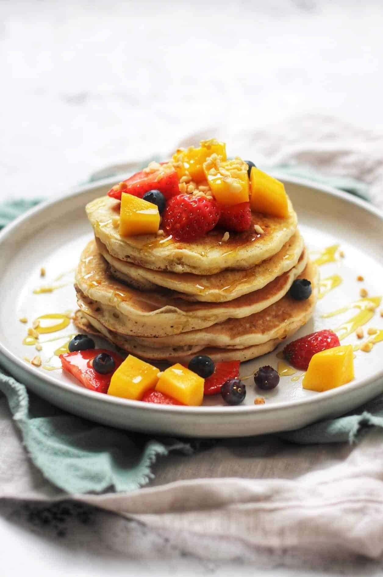 Een stapel pannenkoeken met fruit en siroop op een bord.