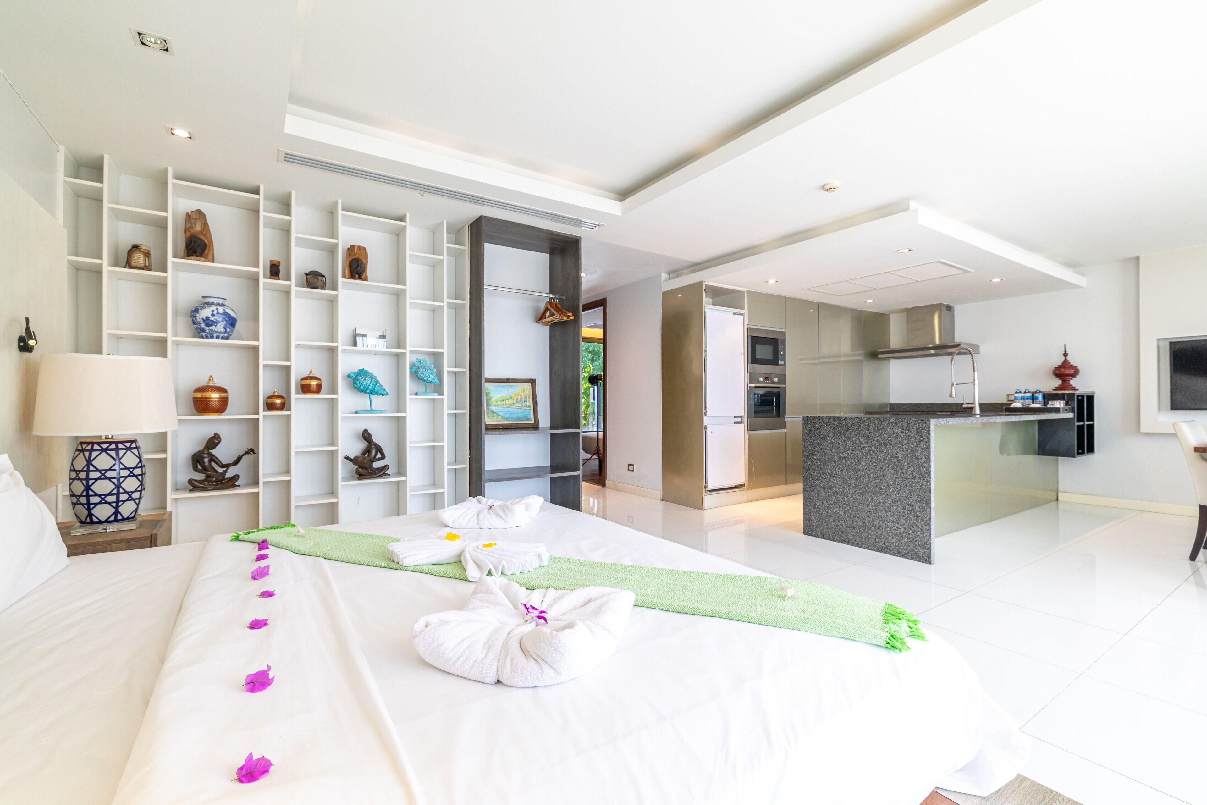 A modern hotel room with a neatly made bed, a green towel, and a wall of decorative items.