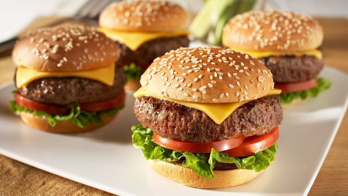 A plate with three cheeseburgers, each with sesame seed buns, lettuce, tomato, and cheese.