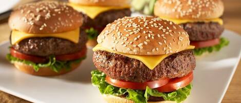A plate with three cheeseburgers, each with sesame seed buns, lettuce, tomato, and cheese.
