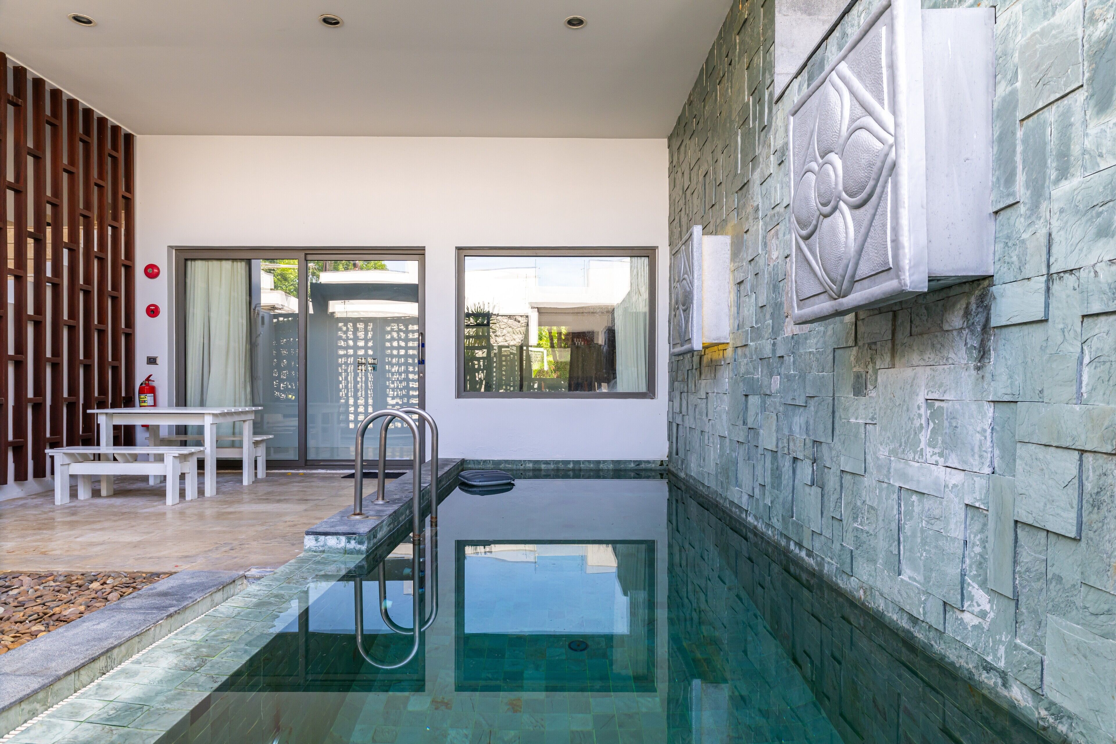 Zona de piscina con muro de piedra, cerca de madera y un banco.