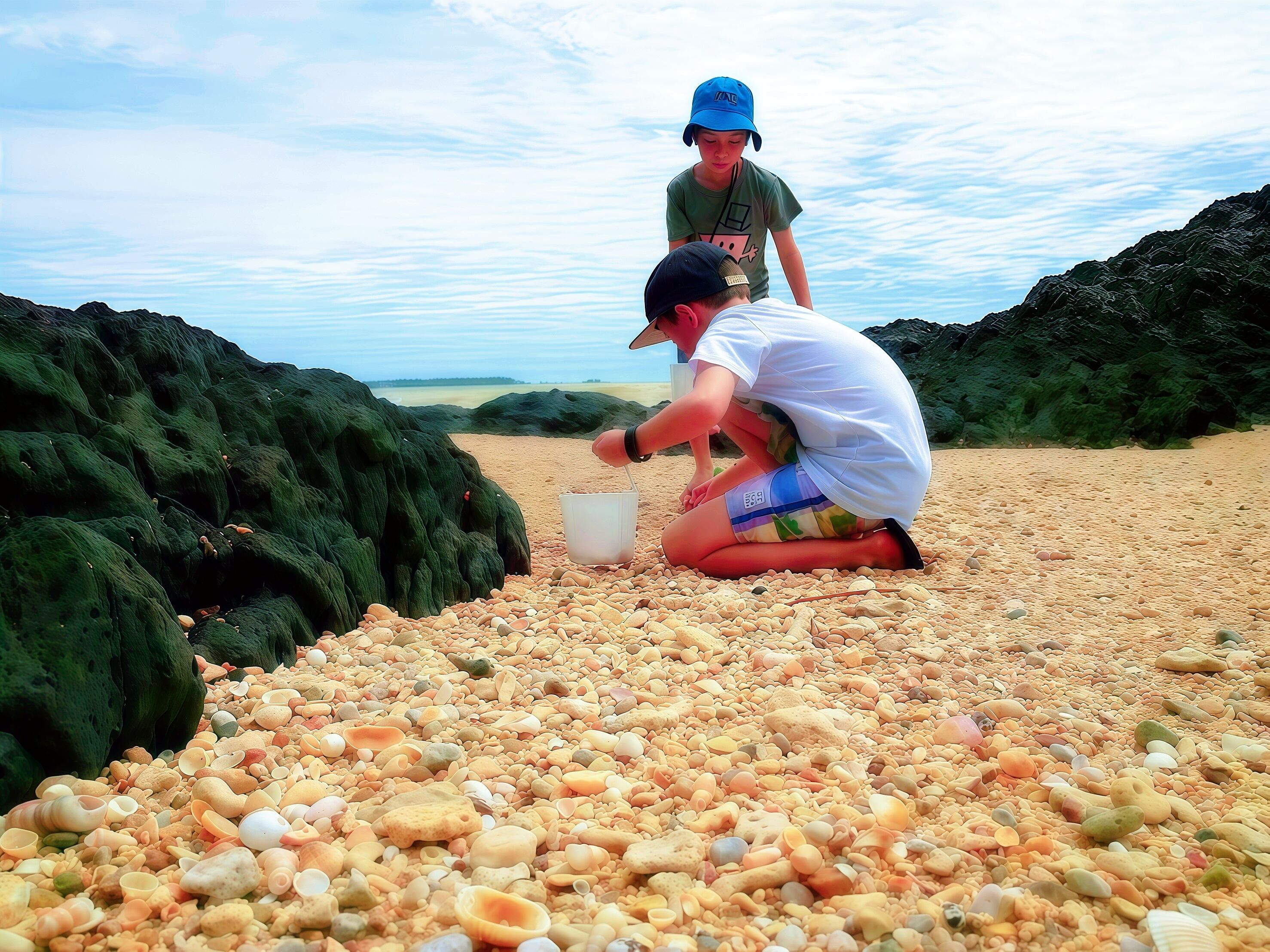 A beach with pebbles and rocks, two people, and a clear sky.