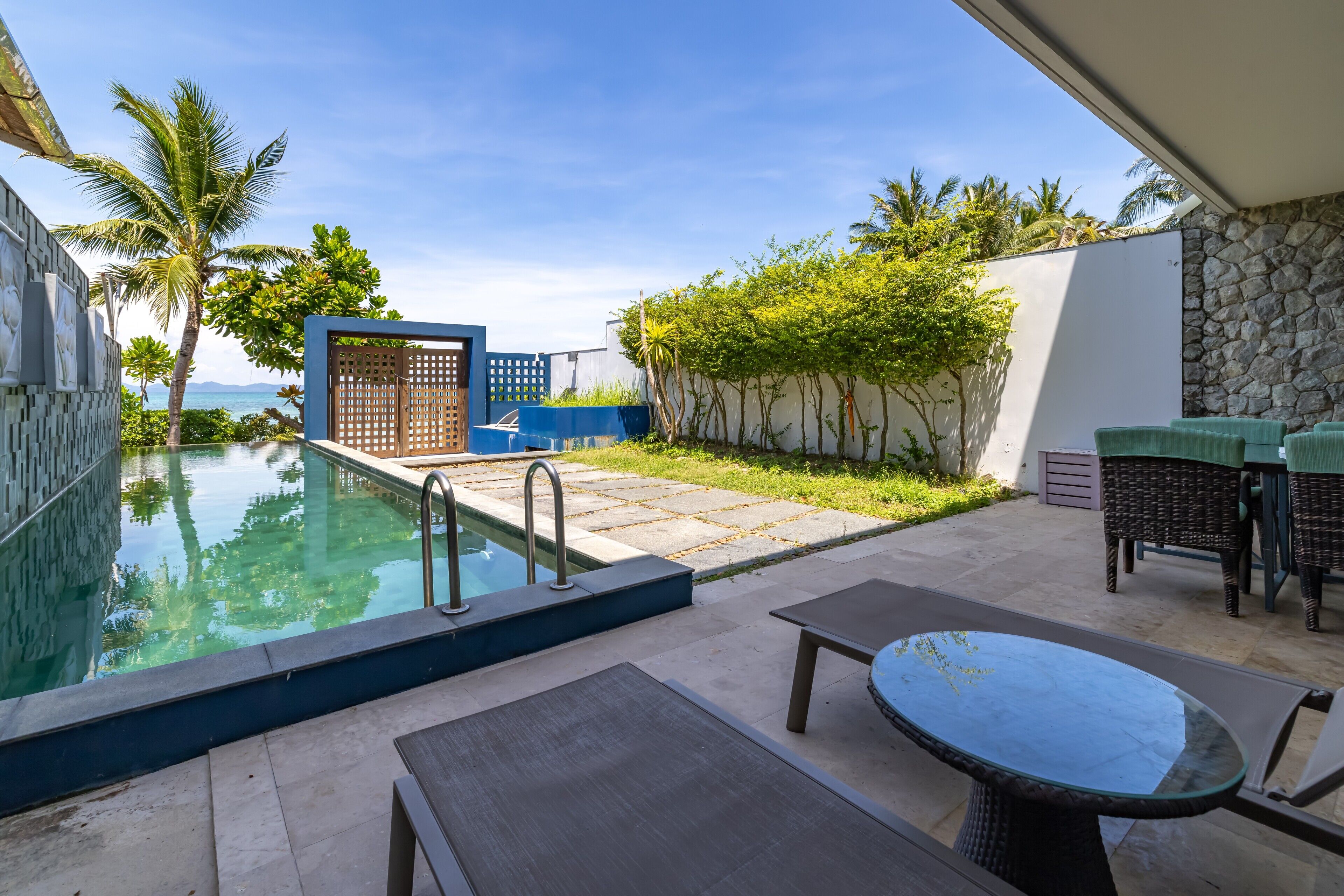 A pool area with a clear view of the ocean, a stone wall, and outdoor furniture.