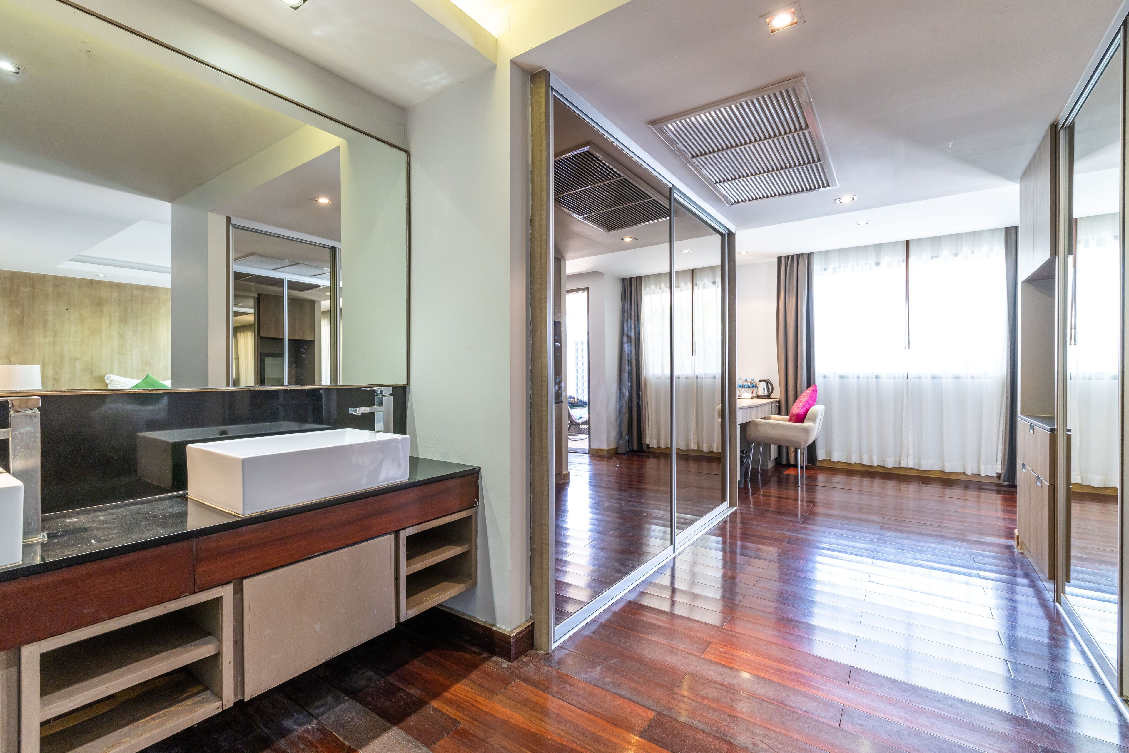 A modern bathroom with a large mirror, a white sink, and wooden cabinetry.