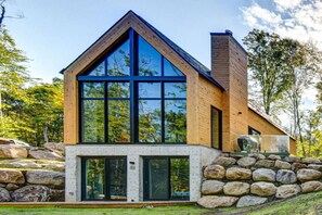 Une maison moderne dotée d’une grande baie vitrée, d’un revêtement extérieur en bois et d’une base en pierre.