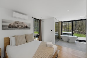 Une chambre moderne avec un grand lit, une photographie d’ours accrochée au mur, une porte vitrée donnant sur une salle de bain équipée d’une baignoire et d’un jacuzzi.