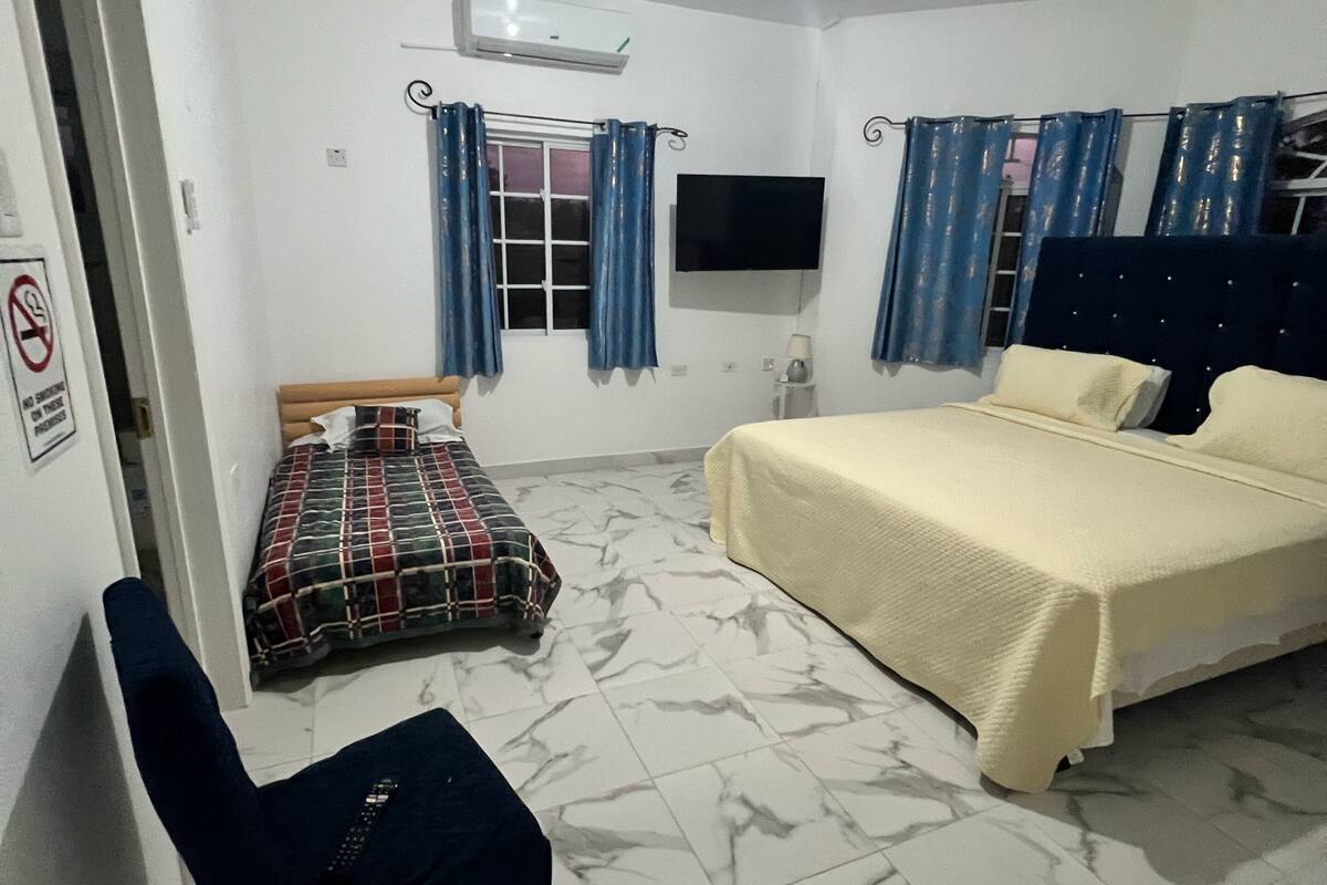 Un dormitorio con cama, una silla, un televisor y una ventana con cortinas.